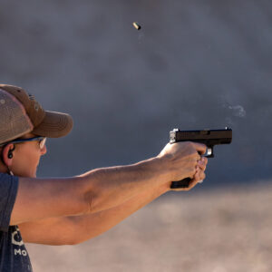 Freezeframe of a student shooting a Glock 17 with smoke coming from muzzle and brass casing in the air.