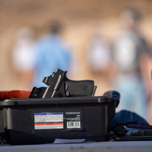 Artistic photo of clear handgun in foreground with students on the firing line in the blurred background.