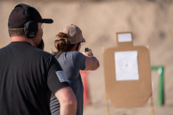 A wife shoots paper targets while her husband looks on, in Ministry of Defense Enhanced Concealed Weapons License class.